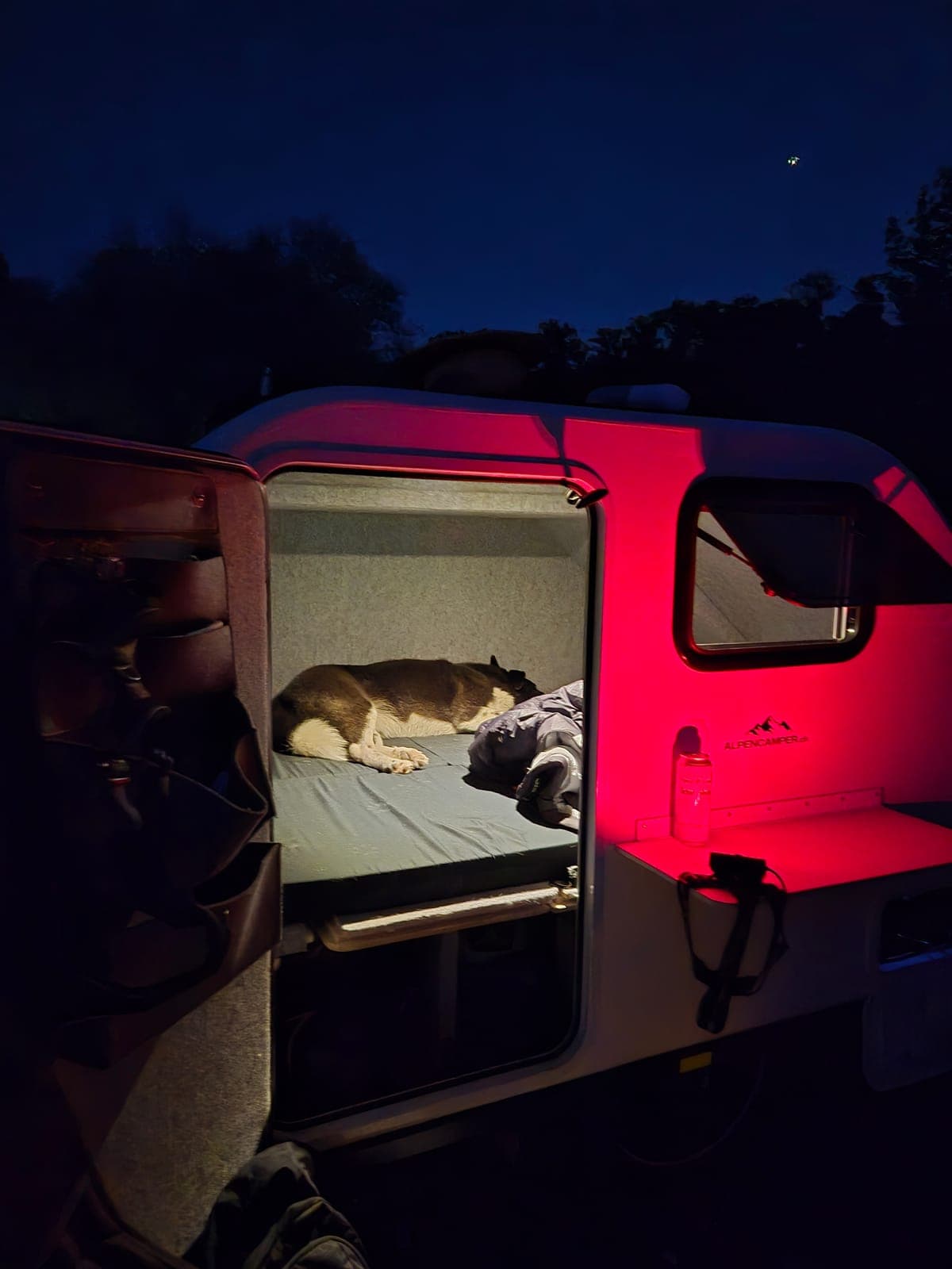 Nachtlager: Der Camper leuchtet rot in der Dämmerung, drinnen schläft Alex schon auf dem Bett